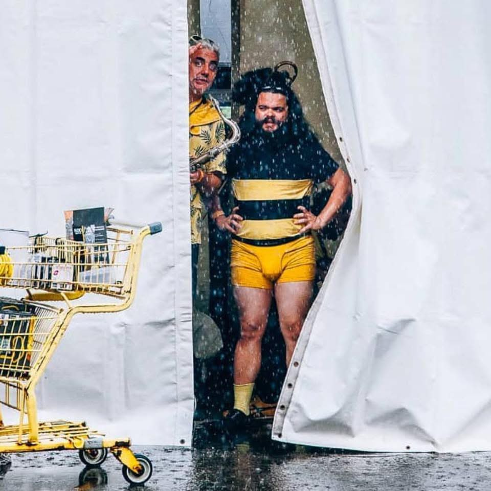 Amayúscula disfrazado de abeja bajo la lluvia, junto a un carrito amarillo